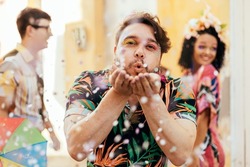 Brazilian Carnival. Young man enjoying the carnival party blowing confetti