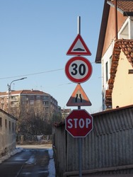 pole with many traffic signs including uneven road, speed limit, road narrows and stop