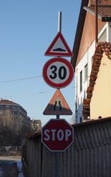 pole with many traffic signs including uneven road, speed limit, road narrows and stop