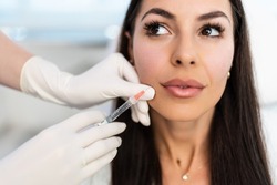 Attractive woman is getting a rejuvenating facial injections at beauty clinic. The expert beautician is filling female wrinkles with botulinum toxin injections or hyaluronic acid fillers.