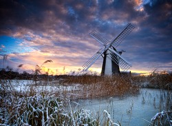 Norfolk windmill in reed bed and fenlands covered in snow with heavy skies