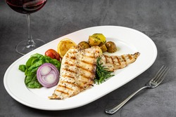 Grilled sea bass fillet with salad and potatoes on stone table