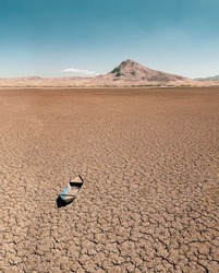 Abandoned row boat on cracked soil on lake bed dried up due to global warming and drought