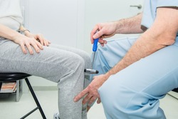 The neurologist testing knee reflex on a female patient using a hammer. Neurological physical examination. Selective focus, close up