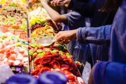 Customers choose sweets from counter with assorted colorful different shape jelly candies on market place in Tel Aviv, Israel. Selective focus, space for text.