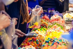 Customers choose sweets from counter with assorted colorful different shape jelly candies on market place in Tel Aviv, Israel. Selective focus, space for text.