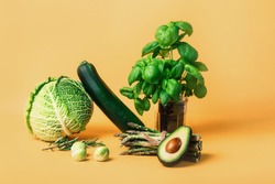 Abstract composition with fresh vegetables of cabbage, zucchini, asparagus, Brussels sprouts, avocado, basil on orange background. Vegetarian and vegan diet. Sustainable lifestyle, plantbased food