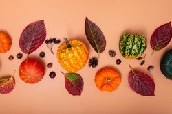 Autumn composition. Pumpkins, dried leaves, nuts and cones on neutral orange background. Autumn, fall, halloween, thanksgiving day concept. Flat lay, top view.