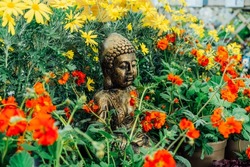 Bronze Gautama Buddha decorative statue in a garden with red and yellow flowers. Exterior, Outdoor Garden decor concept. Selective focus.