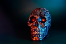 Black human skull decorated with golden points pattern in blue and orange light on dark green background. Halloween decor concept. Selective focus, copy space.