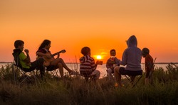 Group of people sitting on the beach with campfire at sunset