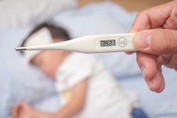 Fever, Close-up medical thermometer, Parent / Father measuring temperature of his ill kid, Asian 3 - 4 years old toddler boy gets high fever lying on bed with cold compress on forehead to cool a fever