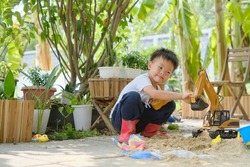 Cute Asian young boy playing with sand alone at home, Kid playing with sand toys and toy construction machinery in backyard home garden , Montessori education, Creative play for kids concept