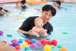 Selective focus of Asian Father take baby boy to swimming class in Thailand, little baby playing colorful toys in the pool, little baby take a swimming lesson with his daddy

