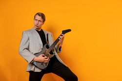 rock ' n ' roll guy, a cool guy with a fake guitar, pretends to play music. Fun and emotion. A young man with a guitar on a yellow background
