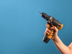 Fix it, fix a malfunction or tighten a bolt on a construction site. A female hand holds a screwdriver or drill, a repair tool, a photo on a blue background.