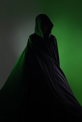 a mystical vampire in a black hoodie. Mysterious figure,face hidden by hood, dark background green backlight