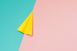 Yellow paper airplane on pastel pink and blue background. Minimal flat lay school concept.
