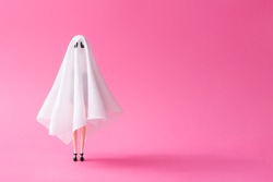 Girl in ghost costume against pastel pink background. Halloween party minimal concept.
