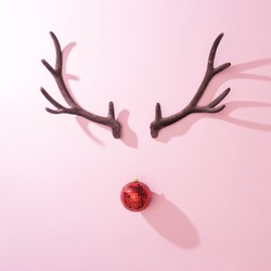 Red Christmas disco ball bauble with reindeer antlers on pink background. Minimal New year Santa concept. Flat lay.