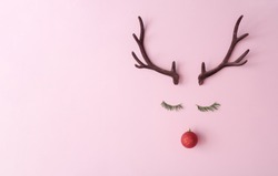 Christmas reindeer concept made of evergreen fir, red bauble decoration and antlers on pastel pink background. Minimal winter holidays idea. Flat lay top view composition.
