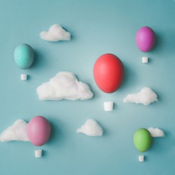 Hot air balloons made of decorated Easter eggs with cotton clouds on bright blue background. Flat lay. Creative concept.