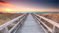 Wooden path at Baltic sea over sand dunes with ocean view, sunset summer evening                              