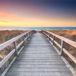 Wooden path at Baltic sea over sand dunes with ocean view, sunset summer evening                                