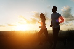 Two athletes running at sunset. Backlit silhouette of man and woman training together.