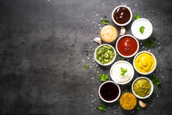Set of sauces - ketchup, mayonnaise, mustard soy sauce, bbq sauce, pesto, chimichurri, mustard grains and pomegranate sauce on dark stone background. Top view copy space.
