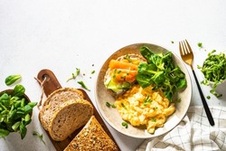 Scrambled eggs, sandwich with cream cheese and salmon and salad leaves at white stone table. Nordic diet. Top view with copy space.