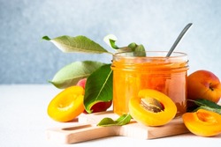 Apricot jam in glass jar at white table.