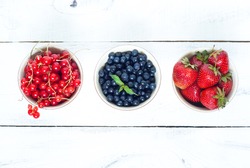 Three little bawls with different berries - strawberry, blueberry and red currants.