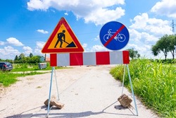 Two signs are set on the road at construction site, triangle sign, work in progress, with red and white stripes and prohibited cycling.