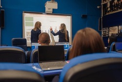 Female university student picked by the professor writing answers on smart board during classes at school.