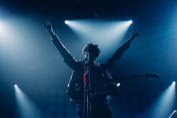 Rock band vocalist silhouette with the guitar singing to microphone with the hands raised up in blue lights
