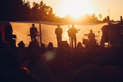 Band playing gig on a beach to the resting people in a warm sunset lights 
