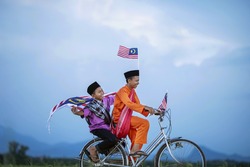 Independence Day concept - Two happy young local boy riding old bicycle at paddy field holding a Malaysian flag