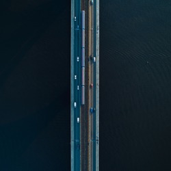 Bridge with two lanes and subway or train rails on a background of dark water. Metro bridge with moving cars. View from above. Aerial view