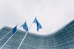 The queue of steeples with blue flags of the European Union against the background of the European Commission building in Brussels, Belgium. EU flag, symbol