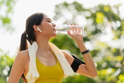 young Woman drinking water from bottle. asian female drinking water after exercises or sport. Beautiful fitness athlete woman wearing hat drinking water after work out exercising on sunset evening