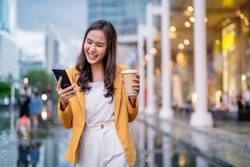 Urban modern lifestyle fashion portrait of asian young female stylish casual Asia woman walking 
with coffee cup and smartphone connection on the street, wearing cute trendy outfit after raining