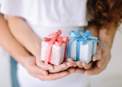 the young family holds a pink and blue gift surprise in hand. young family waiting for baby, hands father and mother keep holding a pink and blue boxes with gifts, newborn boy or girl.