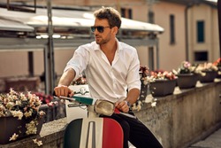 Stylish italian man wearing white shirt and sitting on classic scooter