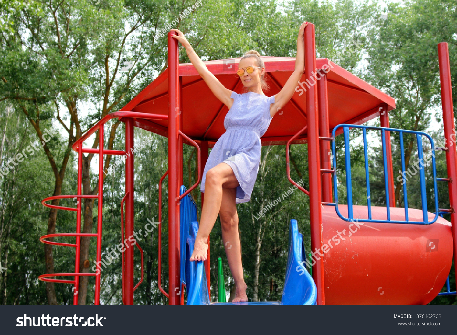https://image.shutterstock.com/shutterstock/photos/1376462708/display_1500/stock-photo-adult-girl-on-the-playground-climbed-an-iron-slide-on-the-background-of-trees-1376462708.jpg