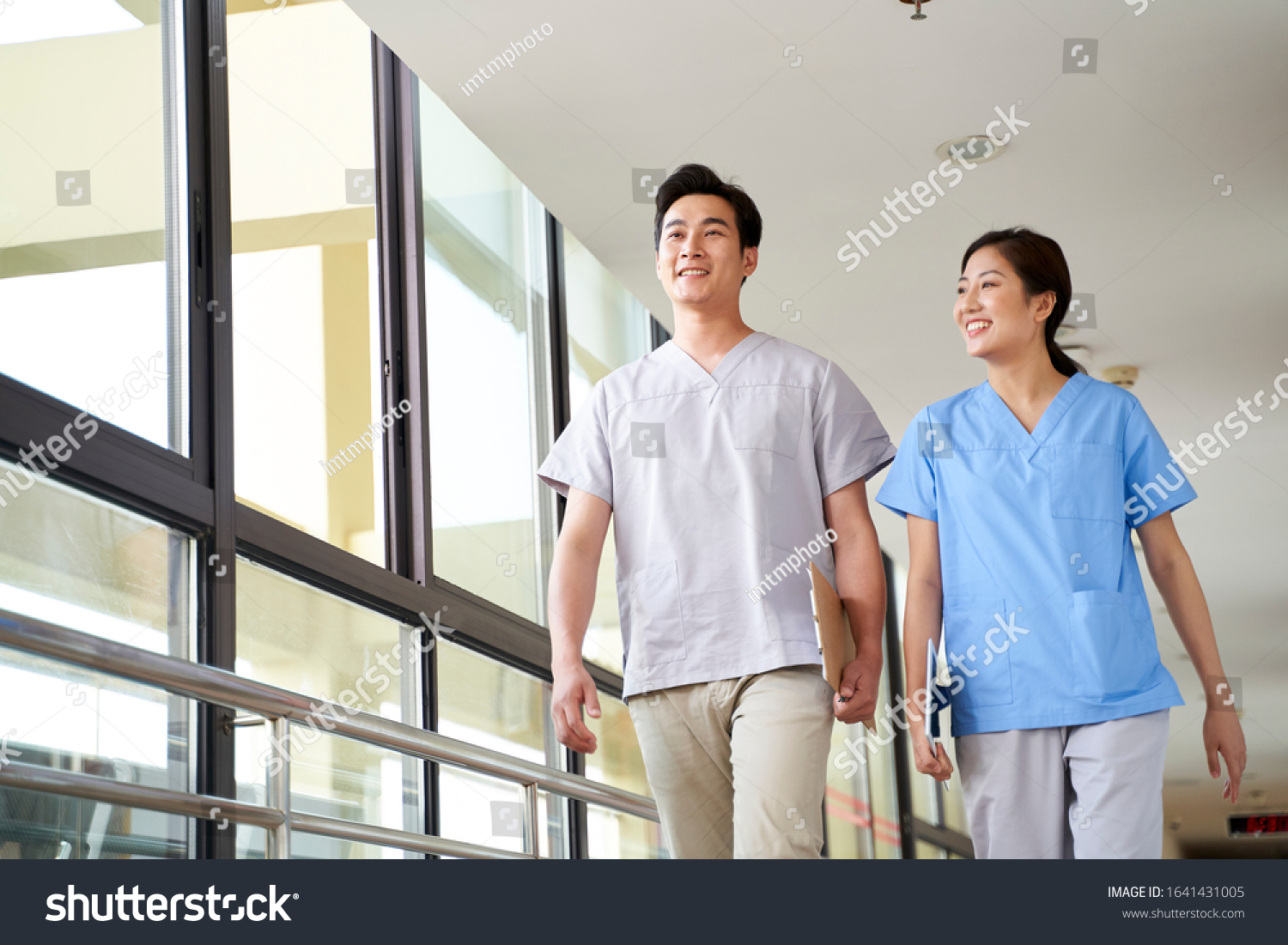 Happy Young Asian Physical Therapists Walking Stock Photo 1641431005   Stock Photo Happy Young Asian Physical Therapists Walking Talking In Hallway Of Nursing Home 1641431005 