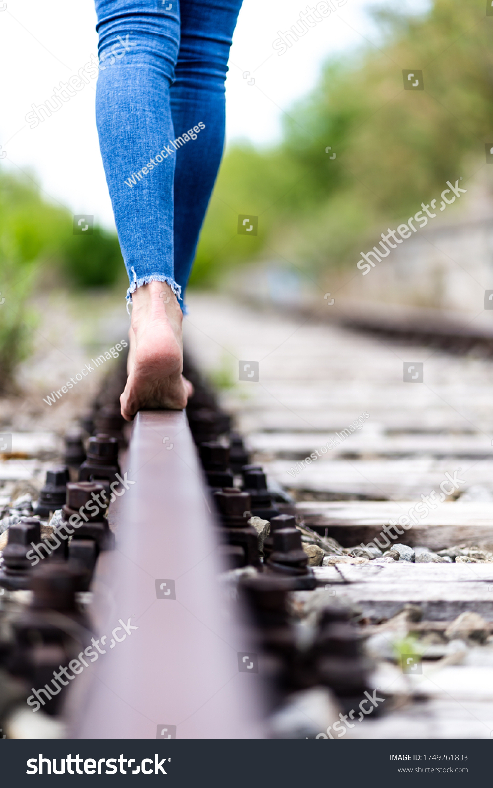 https://image.shutterstock.com/shutterstock/photos/1749261803/display_1500/stock-photo-a-vertical-shot-of-a-female-in-jeans-walking-through-the-train-rails-barefoot-1749261803.jpg