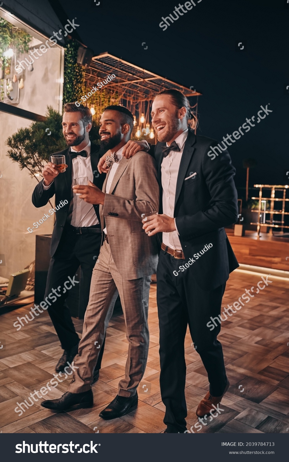 Full Length Of Three Handsome Men In Suits And Bowties Drinking Whiskey