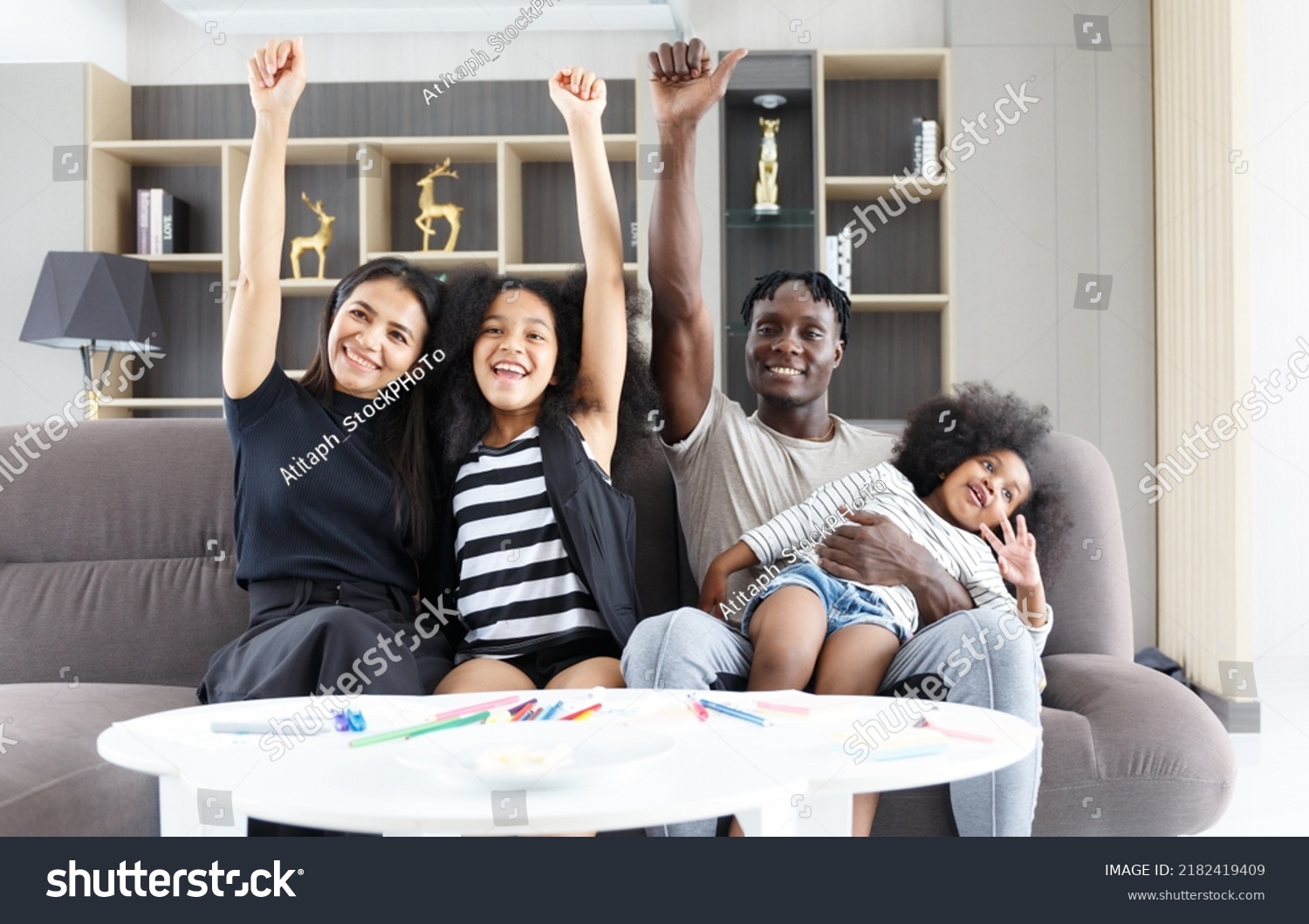 Happy Multiethnic Family Sitting On Sofa Stock Photo 2182419409   Stock Photo A Happy Multi Ethnic Family Sitting On The Sofa With A Cute Daughter Raising Her Hand In 2182419409 