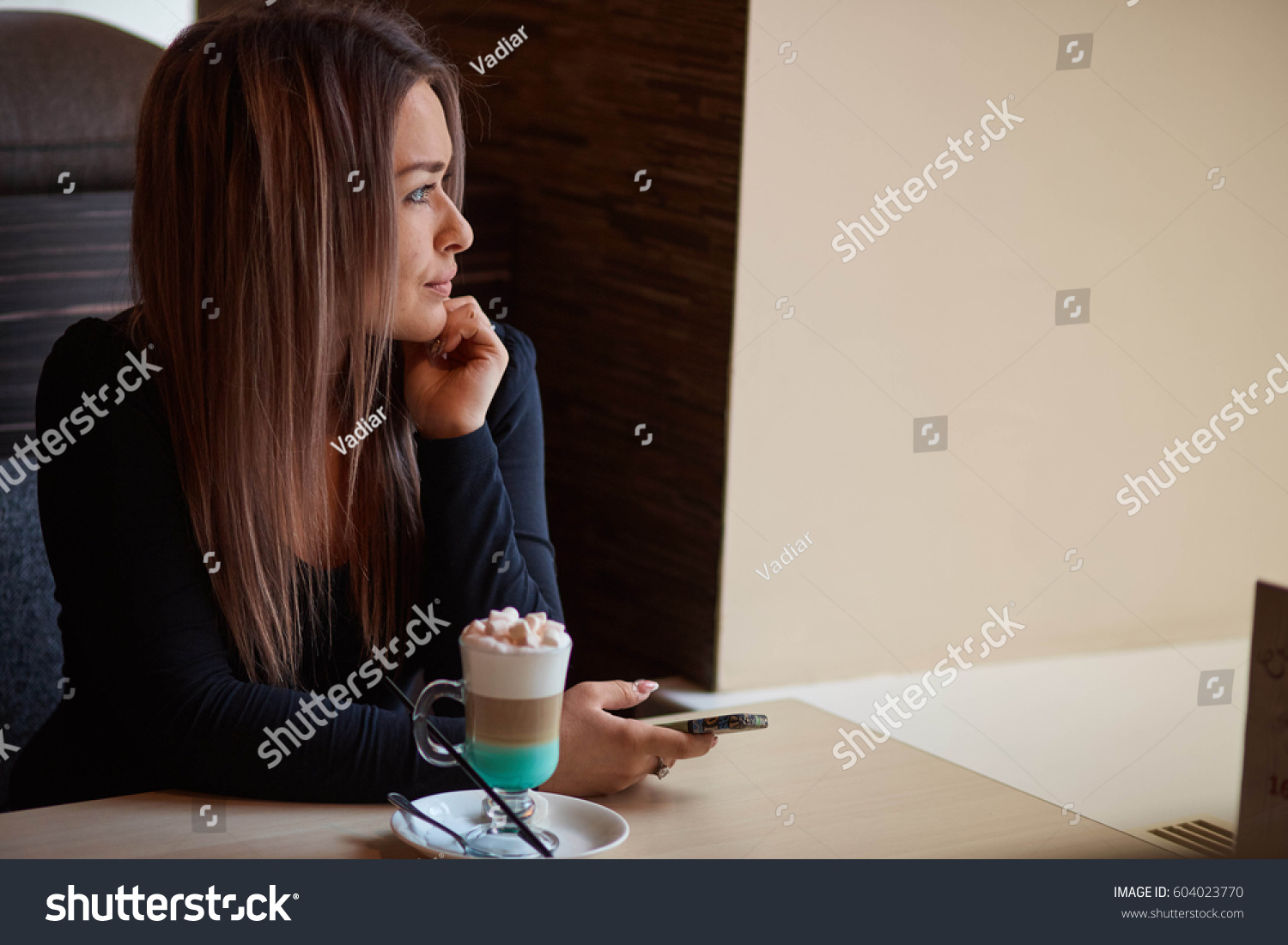 Девушка сидит за столом в кафе в профиль